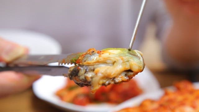 Tongs holding abalone in braised spicy seafood