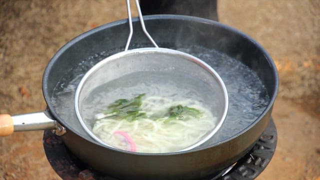 Boiling udon noodles in a pot outdoors