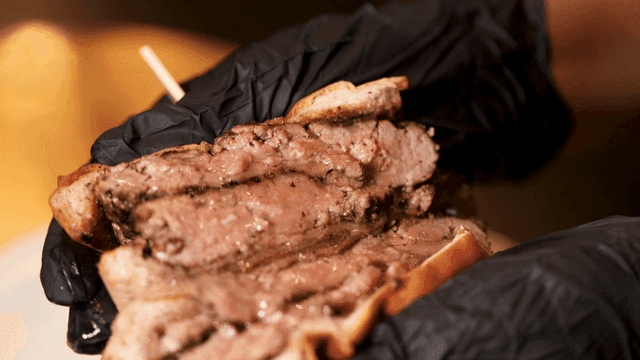 Gloved hand pressing juicy patty-only burger