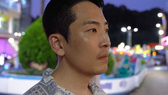 Man standing in front of an amusement park with colorful lights