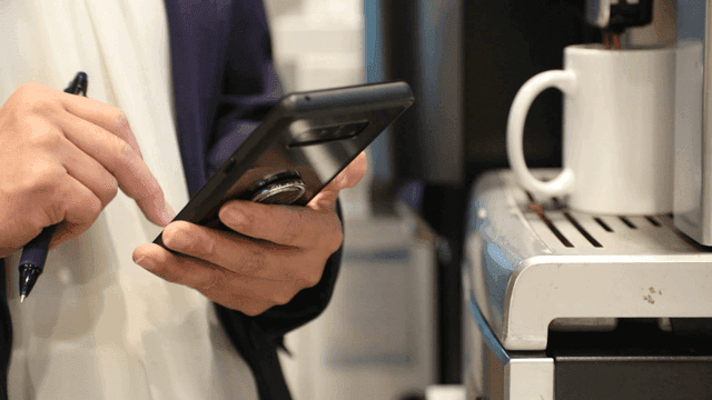 커피 머신 옆에서 스마트폰을 사용하는 사람