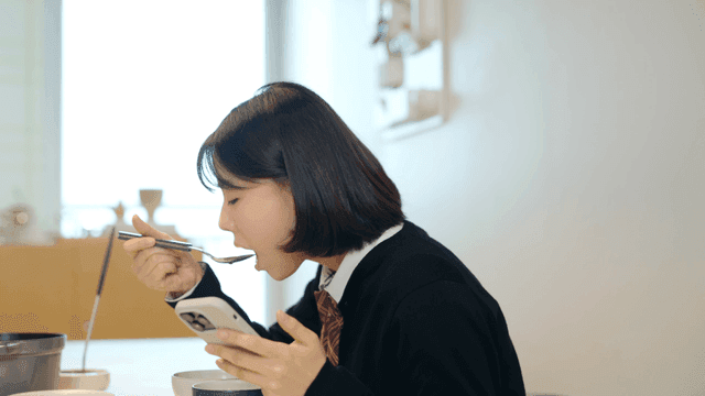 Female high school student eating while using her cell phone
