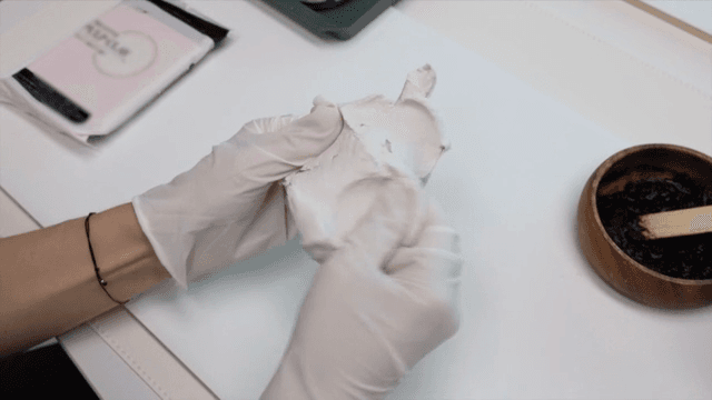 Gloved hands handling clay