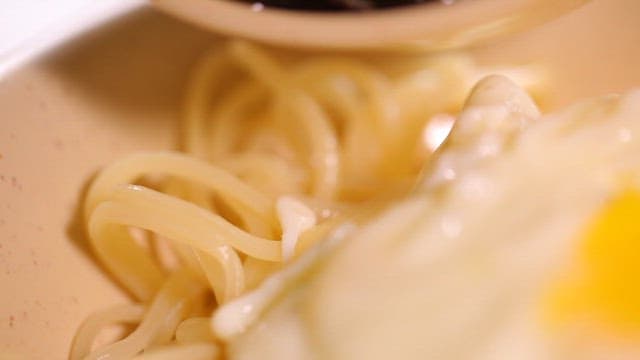 Pouring Jjajang sauce over the noodles with fried egg on top