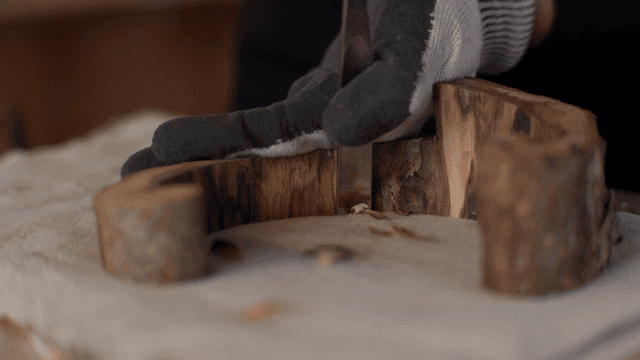 Hands carving wood with a chisel while wearing gloves