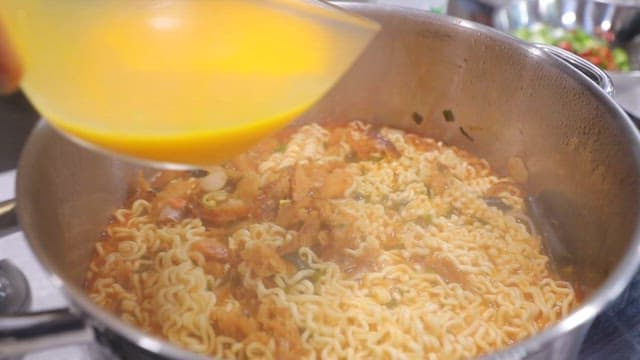 Pour the yellow egg mixture into the ramen while it is cooking in the pot.