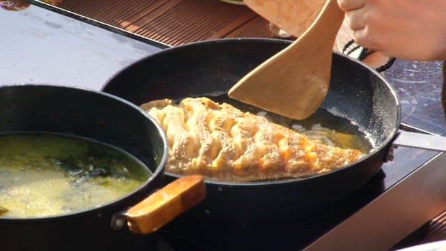 Fish being fried in a pan outdoors