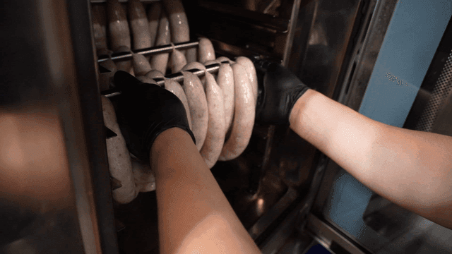 Chef placing sausages onto metal rod in smoker