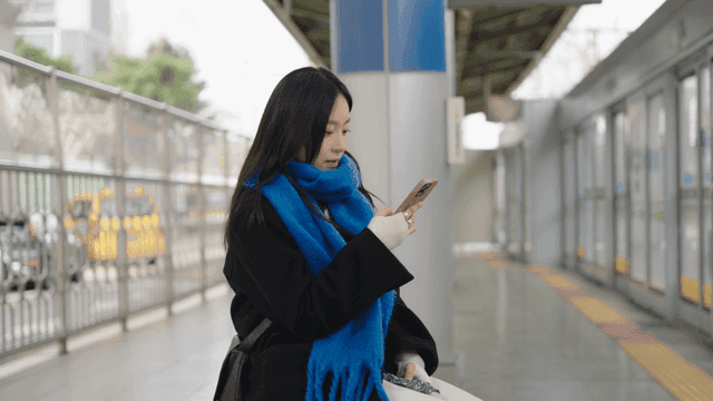 Woman sitting on a bench at a subway station using her smartphone