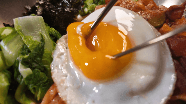 Chopsticks breaking egg yolk on top of bibim kalguksu