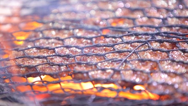 Grilling tteokgalbi sizzling on a grill over charcoal