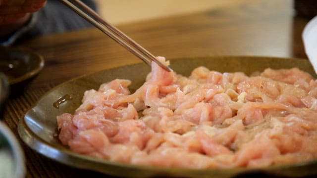 Raw chicken being picked up with chopsticks and placed into the shabu-shabu broth