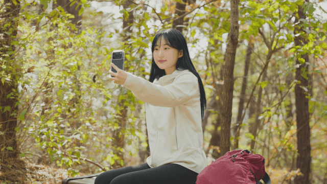Young woman taking selfie on bench in autumn forest