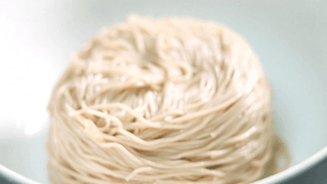 Gloved hands preparing cold noodles in bowl