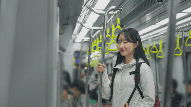 Young woman standing in subway holding seat pole