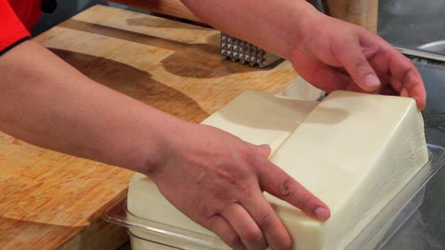 Hands preparing and slicing cheese on a board