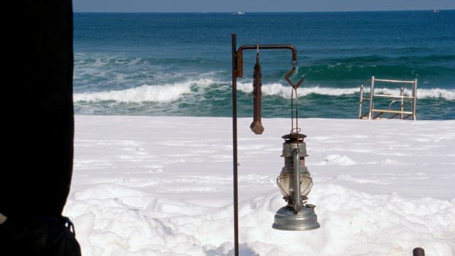 Snow-covered beach with camping lantern and wave background