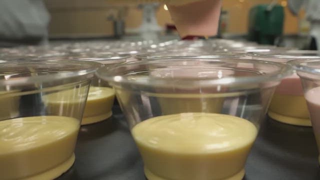 Pouring pink mousse into a plastic container containing yellow mousse