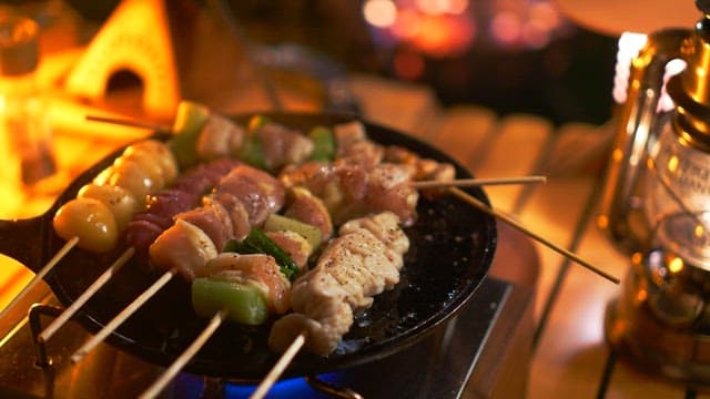 Skewered meat cooking on a pan over a gas burner at night