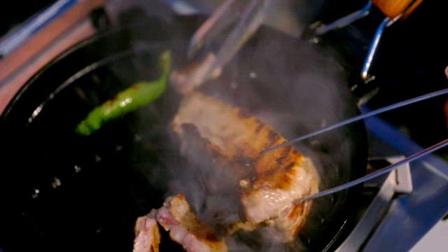 Person cutting grilled pork belly on a pan