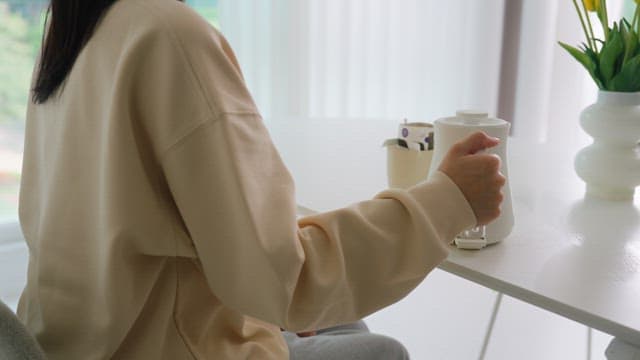 Woman pouring water into cup with coffee pot on table in bright living room