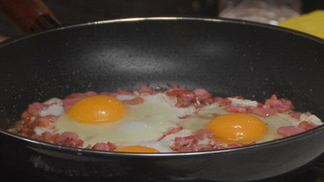 Fried eggs and smoked duck cooked in oil in a frying pan