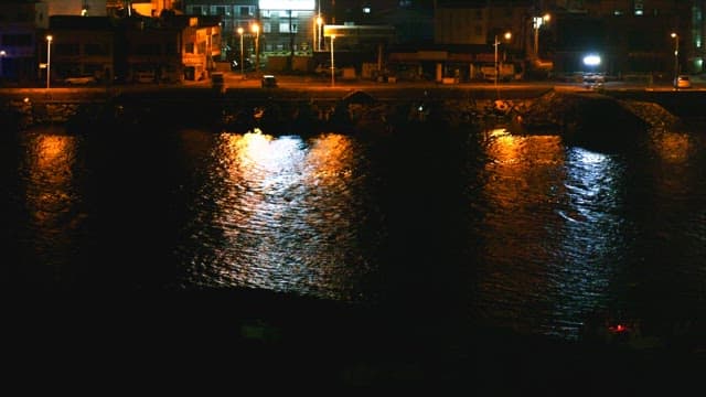 Nighttime view of a coastal city with bright lights reflecting on the water