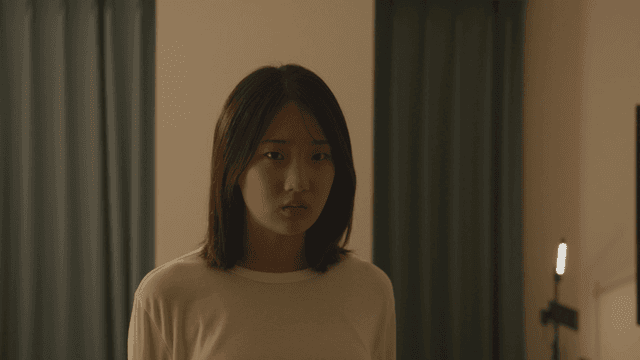 어두운 방에 불안해하며 정면을 바라보는 여성