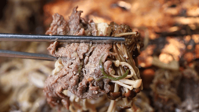 Chopsticks scooping up beef bulgogi with mushrooms