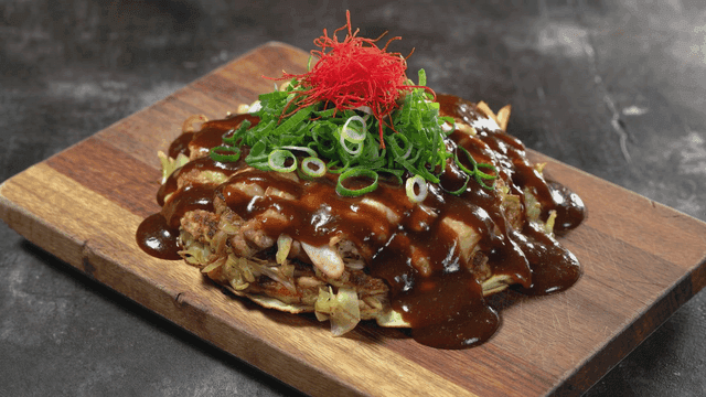 Okonomiyaki topped with sauce and scallions