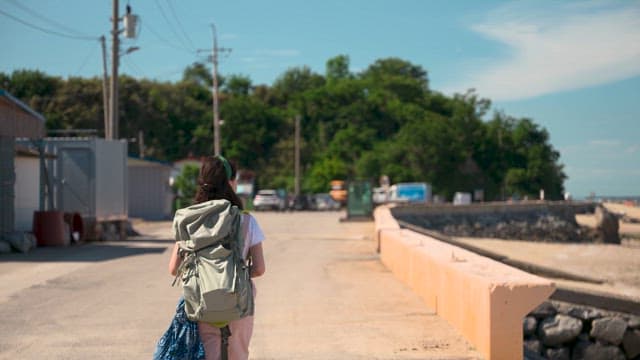 Woman Walking Along a Coastal Road with Backpack