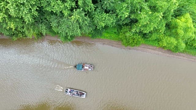 Two boats sailing along a riverside covered with bushes