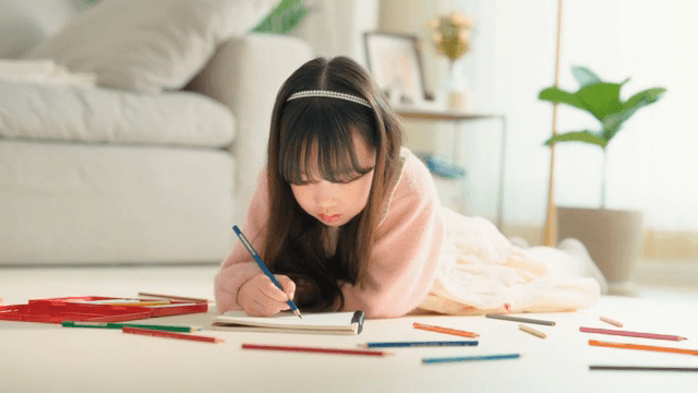 거실에 엎드려 색연필로 그림을 그리는 어린 소녀