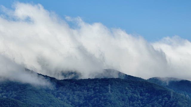 Clouds rolling over a lush green mountain