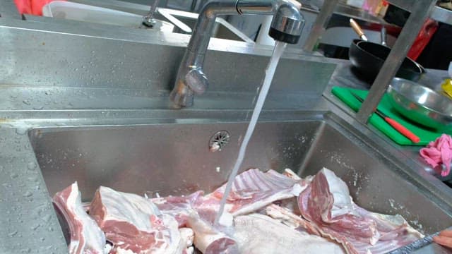 Washing large cuts of meat under running water in a kitchen