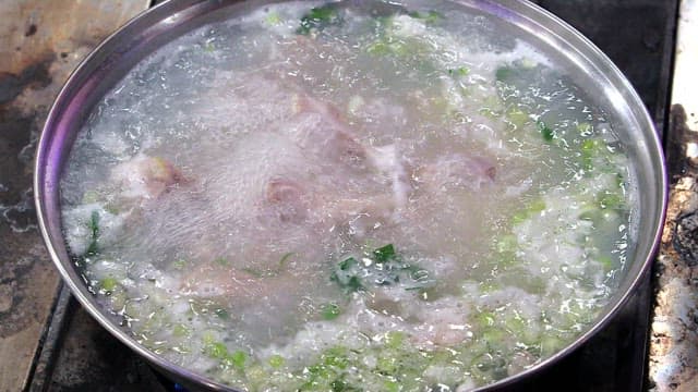 Chicken boiling with green onions in a large pot