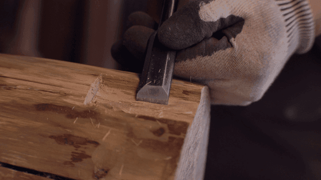 장갑을 낀 손으로 끌을 사용한 목각