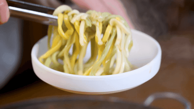 Tongs picking up kalguksu on plate