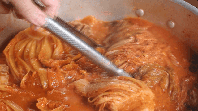 Tongs stirring kimchi stew boiling in pot