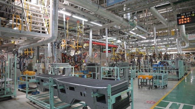 Inside a bustling automotive manufacturing plant with machinery and assembly lines.