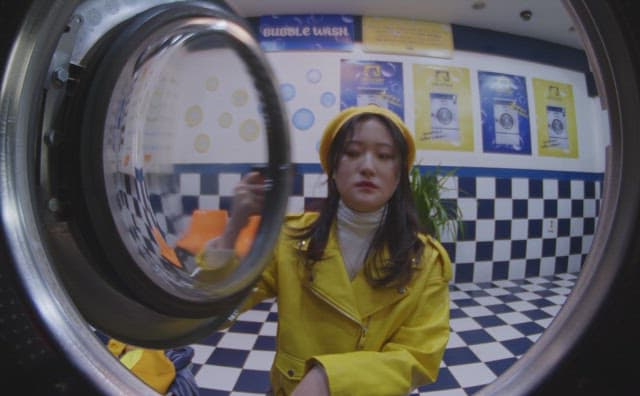 빨랫감을 세탁기 안으로 넣는 노란 옷을 입은 여자