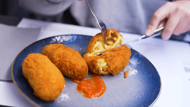 Fork and knife cutting croquette on plate
