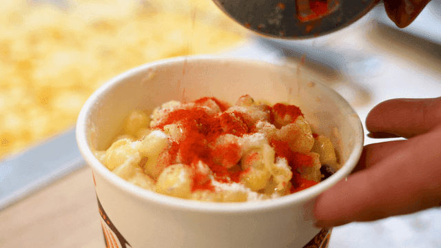 Hand sprinkling paprika powder on buttered corn in cup
