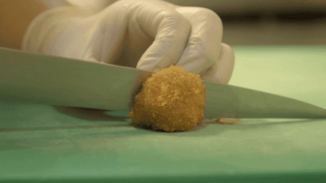 Gloved hand cutting fried croquette