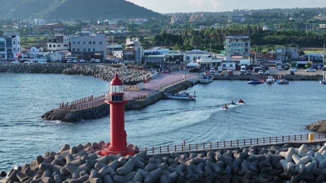 Coastal harbor town crowded with people enjoying water sports and a red lighthouse