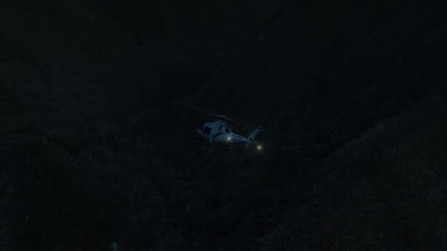 Helicopter Flying Over a Dark Forest at Night