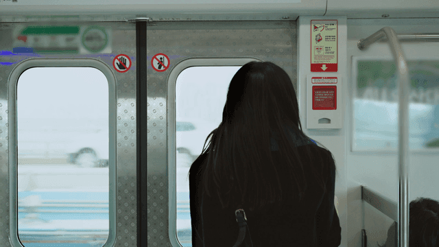 창문넘어 도로가 보이는 전철 안에 서 있는 여성의 뒷모습