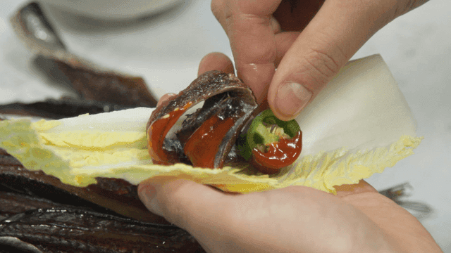 Hands wrapping gwamegi and vegetables in lettuce wrap