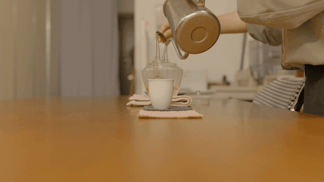Hot water being poured into teapot containing tea leaves on wooden table