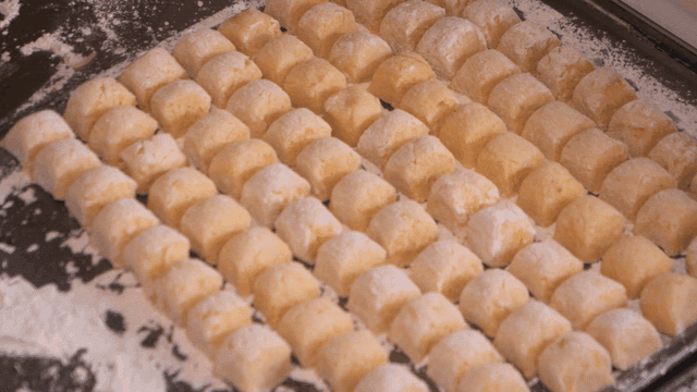 Hands forming dough into small pieces of gnocchi